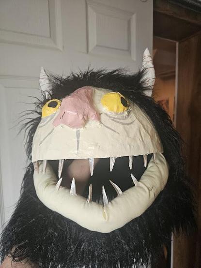 A papier mache monster mask inspired by Where the Wild Things Are, featuring yellow eyes, black fur, and shell teeth