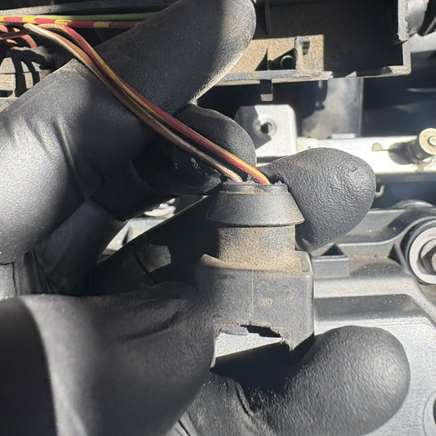 My gloved hand holds up one of the electrical connectors that plugs into the fuel injectors in the M54B30 inline six-cylinder engine in my 2003 BMW 530iT. The plastic on the plug is broken around the edges.