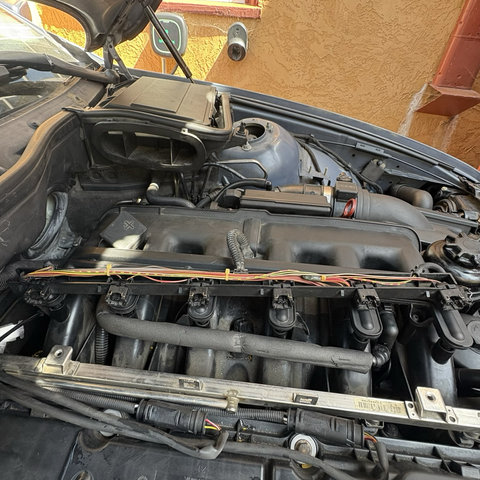 All six fuel injector electrical connectors, freshly replaced with fully intact plastic and metal retaining clips, laid out in their wiring harness box with the top removed, sitting on top of the intake manifold of the engine in my 2003 BMW 530iT.
