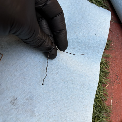 My gloved hand holds a black metal hairpin, bent into a ninety-degree angle, with the tip of the straight edge slightly bent. This is the "tool" I used to remove the wire pins from the plastic connector plugs.