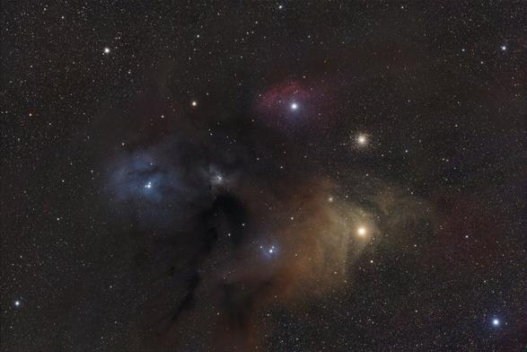 A field of closely packed stars with the frame centered on a large area of gas and dust in the Ophiuchi constellation. There are three obvious clouds of gas: one blue, one red, and one yellow.
