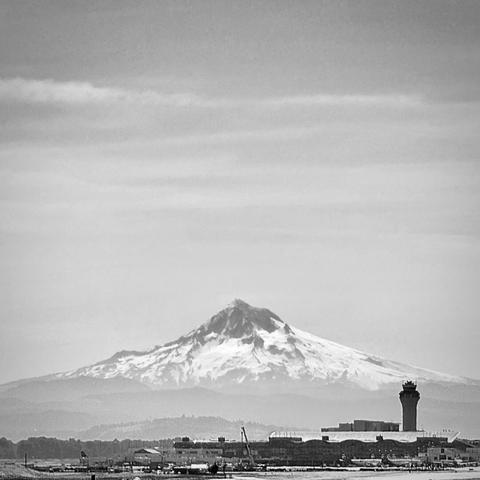 Portland International Airport sits dwarfed in black and white, well below Mount Hood towering high into the distant sky.