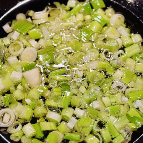 A photo sliced scallion whites in a wok of oil