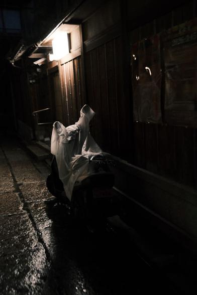 A motorbike is covered with a clear plastic tarp under a lighted sign in Kyoto’s Gion district.