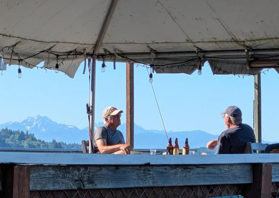 Two men sitting down to. Drink with the Olympic mountains in the background
