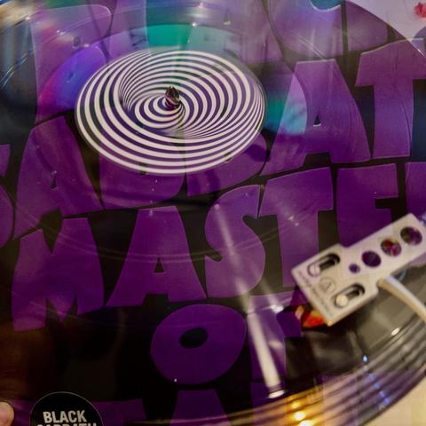 A close-up of a spinning vinyl record featuring a concentric spiral design in the center. The surrounding text is bold and purple, reading "SABAT MASTER". A turntable needle is visible in the foreground.