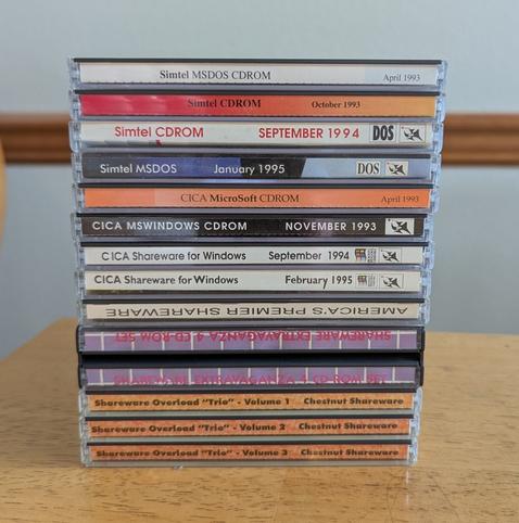 Close-up of a stack of CD-ROM jewel cases, all from shareware distribution sets. Includes Simtel (October 1993), Simtel DOS (April 1993, September 1994, January 1995); CICA (April 1993, November 1993, September 1994, February 1995); "America's Premier Shareware" (2 disc case), "Shareware Extravaganganza 4 CD-ROM SET" (2 disc case), and 'Shareware Overload "Trio" Volumes 1, 2, and 3' from Chestnut Shareware. Some of the Simtel and CICA have the classic "Walnut Creek" wizard logo described in the next photo.
