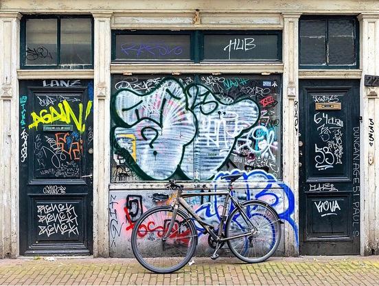 Bicycle parked in front of a graffitied building façade with doors, in a street near Kloveniersburgwal, in Amsterdam, the Netherlands.