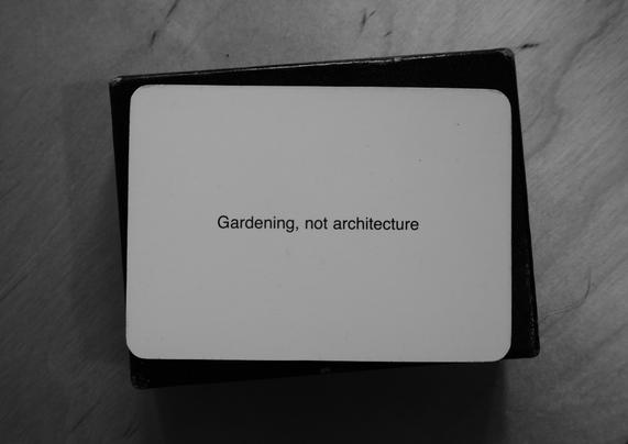 A black-and-white photo of an Oblique Strategy card. The card reads: 'Gardening, not architecture'.
