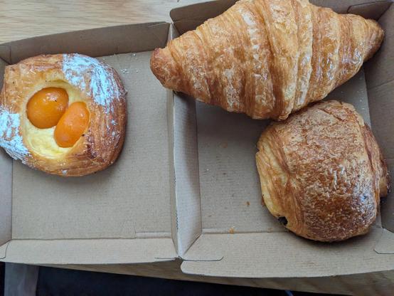 A cardboard food box containing a pain au chocolat, apricot danish and croissant.