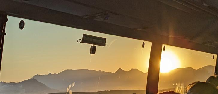 Sun rising over jagged mountain peaks seen through a bus window.