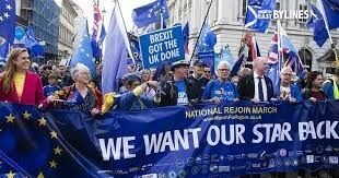 A crowd of individuals strolling along a street, holding European flags in celebration.