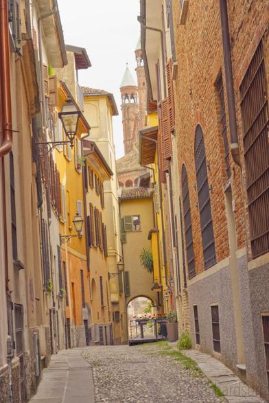 A little street in Cremona, Italy, during the daytime.  Historical buildings line the little street on the right and left.