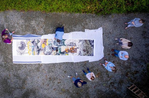 Image: photo from above of eight people – presumably the artists; seven are standing, and one is on hands and knees working on a large tapestry spread out on gravelly ground • “Featuring work by Muriel Beckett, Tish Canniffe, Frances Crowe, Pascale De Coninck, Lorna Donlon, Terry Dunne, Catherine Ryan, and Heather Underwood    Artists Talk: Friday 30 May, 11am • The talk will include presentations by each artist as well as a private viewing of the Timelines short film made by Crannog Media.    Wexford County Council Arts Department is excited to present Timelines: Growth and Catastrophe, a touring exhibition of fibre art which launched in 2024 as part of Culture Night celebrations at Roscommon Arts Centre. This captivating exhibition, which has toured nationwide, showcases the third collaborative work from the Timelines Tapestry Group—a talented collective of weavers and tapestry artists. It will run at Wexford County Council from Friday, 30th May to Friday, 11th July, 2025…”