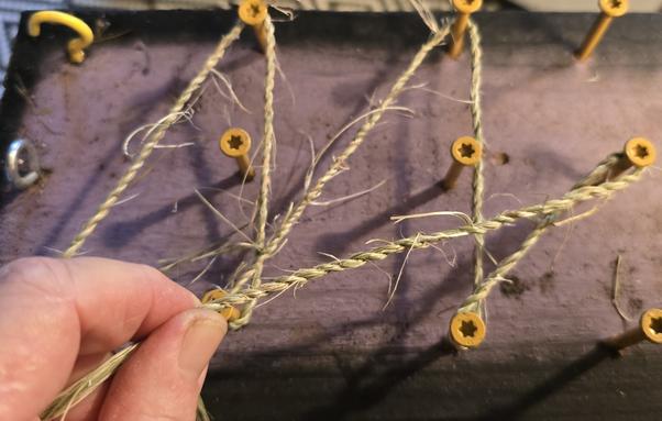 Hands twisting sedge fiber into cordage. It is twined around a home made cordage and lei making board.