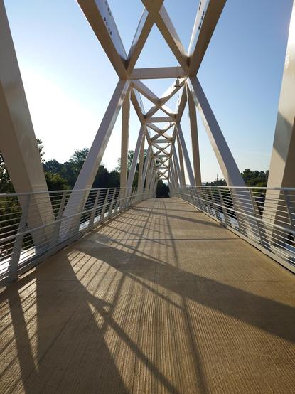 A modern pedestrian bridge with geometrical shapes.
Trees at the bottom.
Sunny weather