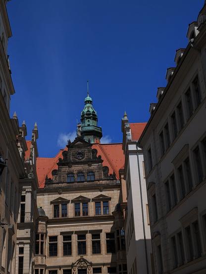 Es ist eine Häuserwand mit Fenstern zusehen, dahinter blickt ein Kirchturm hervor.