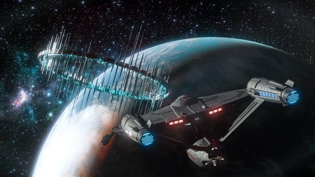 The USS Enterprise from Strange New Worlds flies through space toward a massive cylindrical space station orbiting a planet. The Enterprise has its distinctive angular design with glowing blue engine exhausts and red accent lights along the hull. The enormous orbital structure features tall vertical spikes or towers extending from it, illuminated by blue lights. Below, a planet shows swirling blue and white atmospheric patterns. The scene is set against deep space filled with stars and colorful nebulae creating pink and blue cosmic clouds in the background.