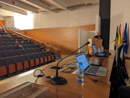 Lecture hall with laptops and microphones and a Spanish, Andalusian and EU flag behind