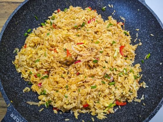 W podobnej trochę do woka patelni znajduje się usmażony ryż z widocznymi czerwonymi paskami papryczki chilli, zielonym szczypiorem i blado-fioletowymi szalotkami.
