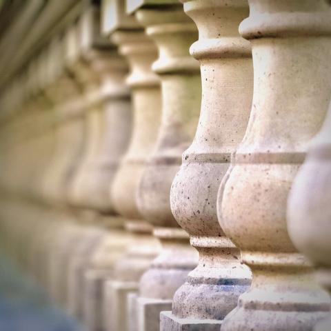 Short, thick, beige stone columns support a large, concrete handrail, as they fade off into the distance.