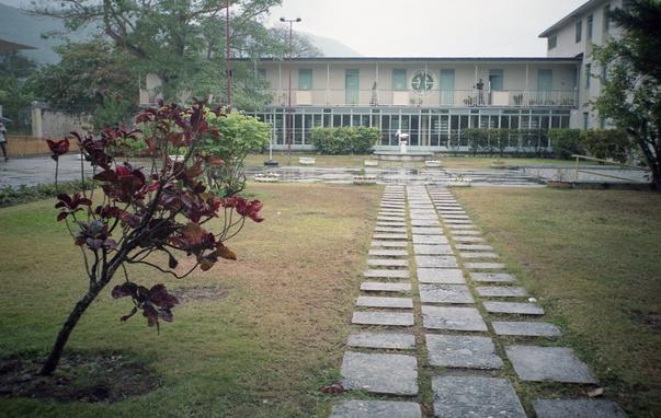 Outside the dining hall. Overcast day, large lawn and sidewalk leading to a long, flat building. Wonderful smells of food cooking, I seem to remember it even the smell of wood fire