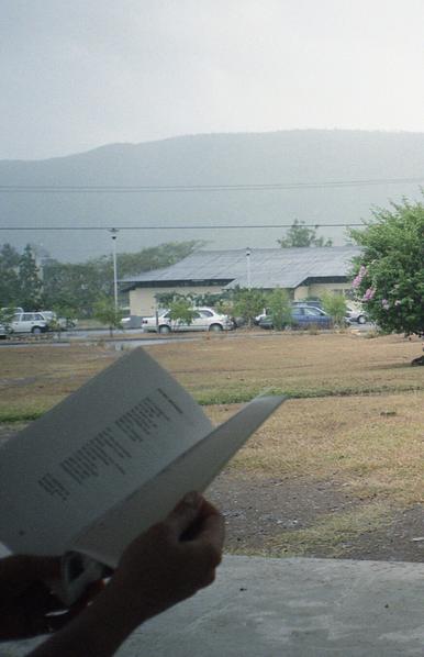 Waiting while reading a book of local poetry, in the foreground against a hilly background