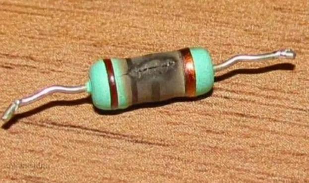 A photo of a blackened resistor between two wires, burned out