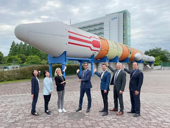 Vor der japanischen Raumfahrtbehörde JAXA (Japan Aerospace Exploration Agency). Zu sehen ist im Hintergrund eine H-2-Rakete.