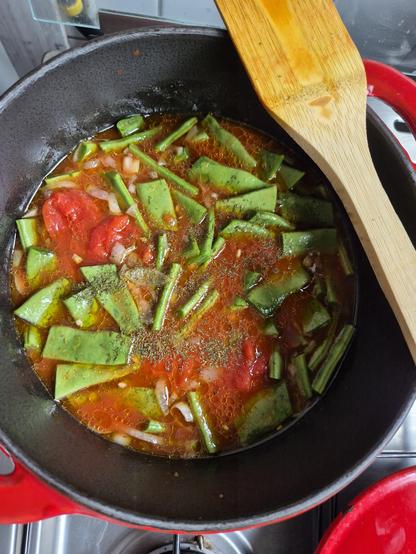 Bovenkant pan met grove stukken felgroene snijboon, gepelde tomaten en sjalot erin, met veel olie, en dille bovenop, roerspaan balancerend op de rand.
