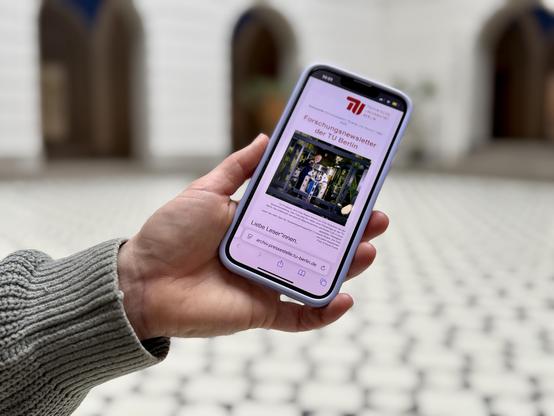 eine Hand hält ein Handy, auf dem der Forschungsnewsletter der TU Berlin angezeigt wird. Foto: Anna Groh