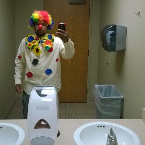 Un homme déguisé en clown se prend en selfie dans le miroir de toilettes publiques, signifiant que la personne qui travaille pour l'Elysée est un clown.