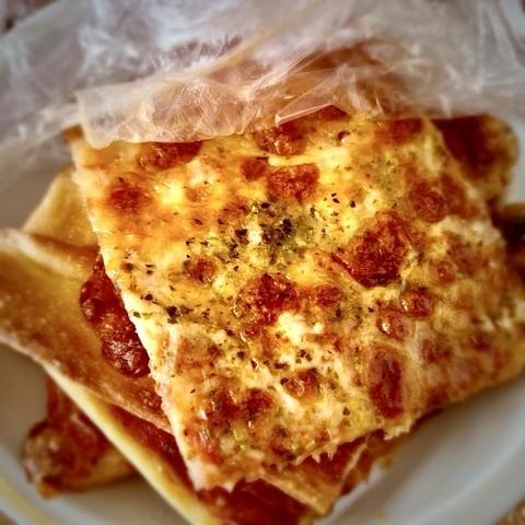 Ein Teller mit mehreren Pizzastücken mit geschmolzenem Käse und Kräutern, einige Stücke sind teilweise noch mit Plastikfolie bedeckt.

A plate containing several pieces of pizza topped with melted cheese and herbs, some pieces are partially covered with plastic wrap.