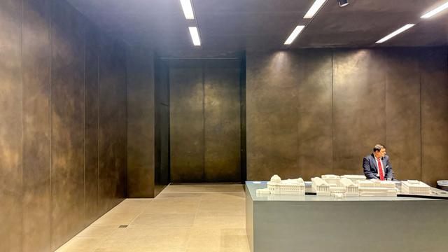 Ein Museumswärter sitzt in einem dunklen Ausstellungsraum vor dem Modell des Museums und wie er da sitzt, wirkt er wie ein Teil des Modells, finde ich zumindest