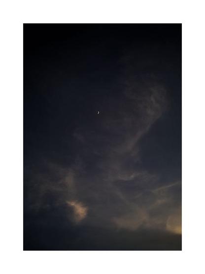 The crescent moon resting in a vast, shadowy canvas of dusk clouds evokes a sense of solitude and quiet wonder. The minimalism and soft fading light draw the viewer inward.