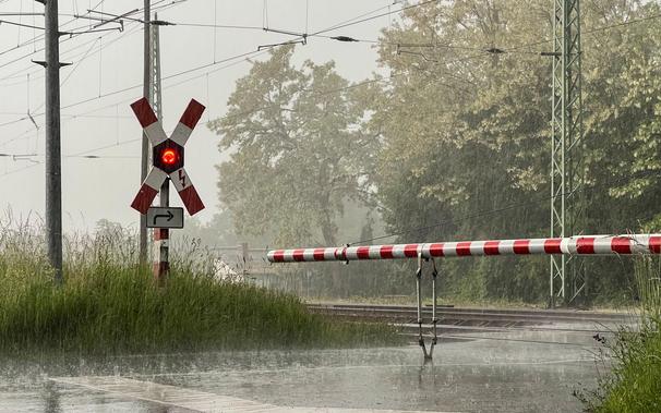 Blick auf einen geschlossenen Bahnübergang mit neuem Schrankenbaum und WSSB Andreaskreuz. Es ist düster und regnet stark.