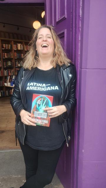 Argentinian author Agustina Bazterrica laughing in the doorway of the Edinburgh Bookshop, while holding a copy of her new novel, The Unworthy