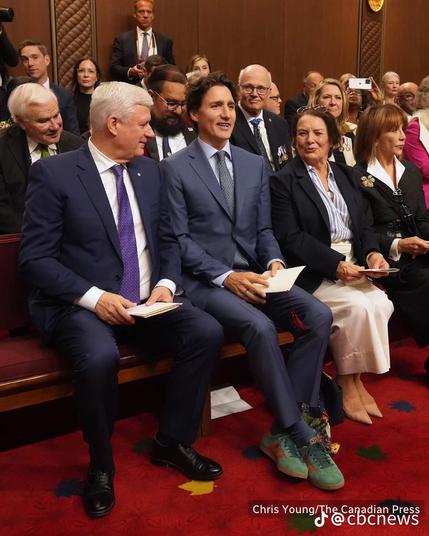 Former Canadian Prime Minister Stephen Harper sits leftmost next to former Canadian Prime Minister Justin Trudeau and Trudeau's mother among many guests present to hear head of state King Charles personally make the Speech from the Throne to open the new Canadian Parliamentary session in Ottawa, Canada.

Guests are seated on dark wooden pew-like benches atop a deep red carpet adorned with maple leaves. The leaf directly under Harper's left foot is bright yellow, appearing to be a cheese slice.

Photo: Chris Young, The Canadian Press (CP)