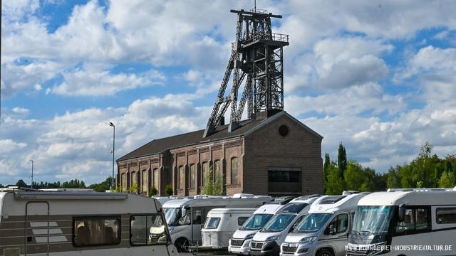 Historisches Fördergerüst einer Zeche mit Backsteingebäude und Wohnmobilen im Vordergrund