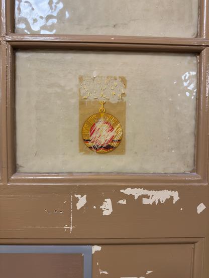 Eike der Türen. In einem Fenster, was von hinten abgedeckt ist klebt ein DDR Wappen, bei dem jemand die Mitte etwas angekratzt hat, damit es nicht mehr sofort erkennbar ist.