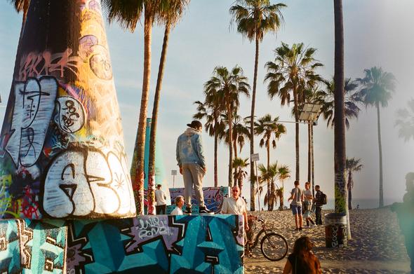 A young person stands on a graffiti painted concrete structure during sunset in Venice Beach. Others look up at the person from below. 

Source text: https://www.visitveniceca.com/2021/11/01/venice-fun-facts/
https://venicechamber.net/2020/01/08/venice-coin-toss/