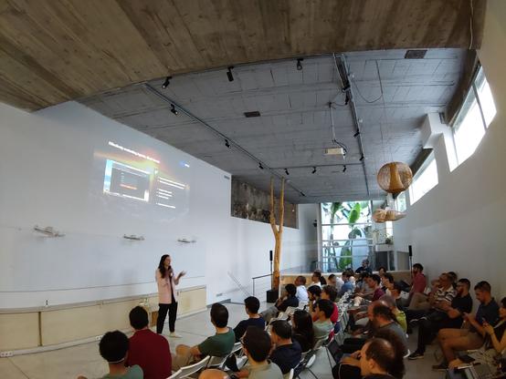 Foto ojo de pez de un espacio con techo alto, gente en sillas en disposición "teatro"
