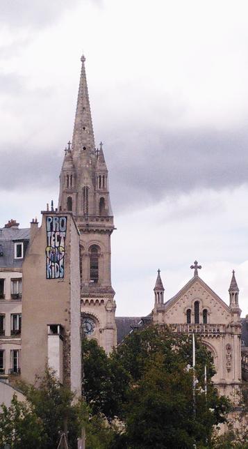 Inscription "Protect trans kids" sur le pignon d'un immeuble, avec en fond l'église Saint-Ambroise