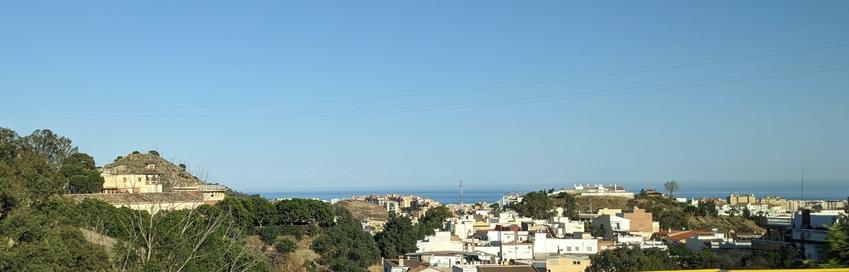 Distant view of white houses and green hills before a blue Mediterranean sea.