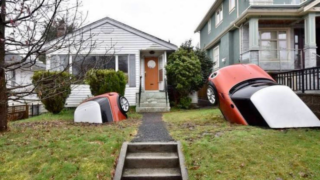 Two Mini Coopers half-buried in the front yard of a house.