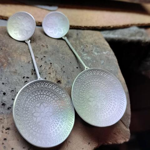 pendientes de plata matizada blanca.
parte superior de circulo de 1 cm con mandala grabado, de ahi cuelga un pequeño palo que conecta con otro circulo de 3 cm de diámetro con un mandala mas grande grabado