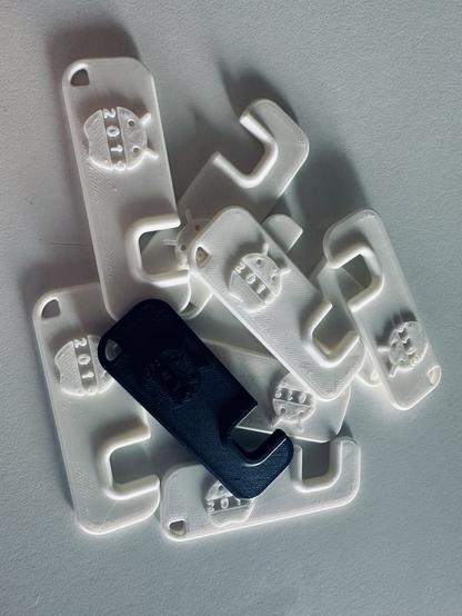 3D-printed phone stands. They're rectangular with a notch to hold your phone so it's tilted to landscape orientation. There are white ones and one black one. Each one features a logo consisting of a Bugdroid head (Android's mascot) and the bottom of an apple (Apple's logo), with the year 2019 next to it.