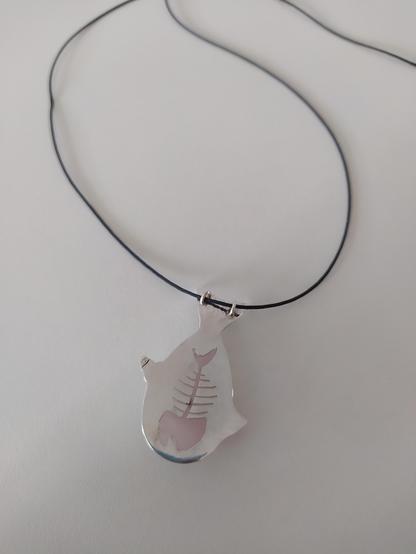 the back side of a silver fish shaped pendant with black cord. it has a fishbone shape in this side