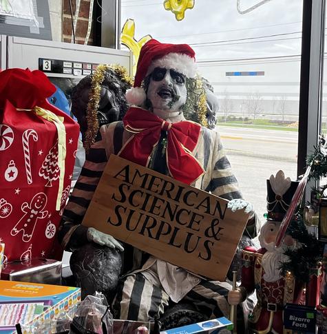 Life sized Beetlejuice manikin in a Santa hat holding an American science and surplus sign