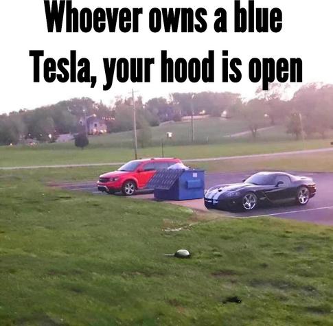 "Whoever owns a blue Tesla, your hood is open." Two parked cars with a blue dumpster between them.